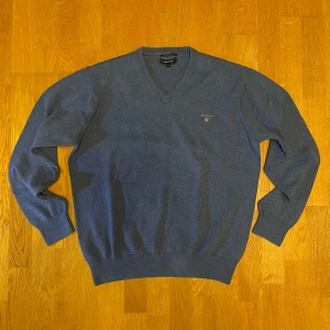 Blå Gant tröja - Säljer nu en blå v-ringad Gant tröja. Tröjan är i storlek L. Kan mötas upp i södra Stockholm. Tröjan är i fint skick och är gjord av premium cotton. Var inte rädd för frågor!