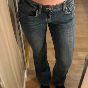 Blå bootcut jeans med kontrastsömmar - Snygga blå jeans med bootcut-modell och låg midja. Jeansen har tydliga vita kontrastsömmar på bakfickorna och klassisk femficksdesign. Tillverkade i jeansmaterial med en lätt tvättad look. Det står storlek 38 men den sitter som 36.  Perfekta för dig som gillar en avslappnad men trendig stil.