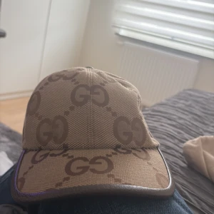 GG Keps - Snygg keps i beige och brunt med det klassiska GG-mönstret över hela kepsen. Justerbar rem baktill i brunt skinn och detaljer i canvas. Perfekt accessoar för att lyfta din outfit med en lyxig touch.