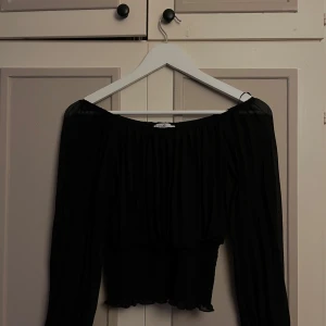 Svart offshoulder topp  - Säljer en svart offshoulder topp från Hailys med långa ärmar och smockad midja. Toppen har en luftig, plisserad look upptill och sitter tajt nedtill med volangkant. 