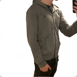 Ralph Lauren Hoodie - Tja säljer nu en riktigt snygg Ralph lauren hoodie i storlek M och i färgen Grå i performance material. Hoodien är i ett fint skick utan några defekter som hål eller fläckar. Nypris 2395kr mitt pris 499kr. Hör av dig vid frågor eller funderingar! Pris ej hugget i sten!
