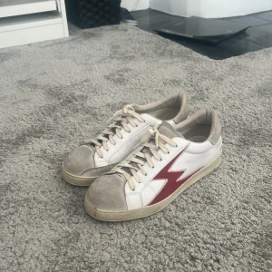 Vit sneaker med röd blixt från Lemon Concept - Snygga vita sneakers från Moa Concept med en röd blixtdetalj på sidan. Skorna har beige mockadetaljer på tån och häl. Nypris 2500 