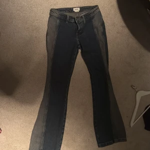 Blå bootcut jeans från Weekday - Säljer ett par blå bootcut jeans från Weekday i storlek 26. Jeansen har en snygg tvåtonad denimlook med mörkare och ljusare paneler längs benen. Klassisk femficksmodell med dragkedja och knapp framtill. Perfekta för en trendig vardagsstil.