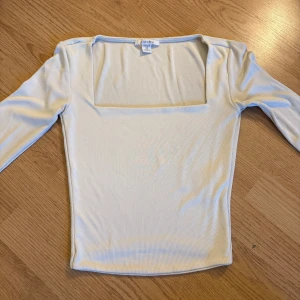 Ljusvit långärmad topp från Amisu - Säljer en stilren ljusvit långärmad topp från Amisu i storlek XS. Toppen har en fyrkantig urringning och är figurnära med stretchigt material. Perfekt att matcha med jeans eller kjol för en clean look.