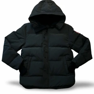 Canada Goose McMillan - Säljer en svart pufferjacka från Canada Goose i storlek M. Jackan har huva, dragkedja framtill och ribbade muddar vid ärmsluten. Klassisk patch på ärmen och diskret logga på dragkedjan. Perfekt för kalla dagar när du vill hålla värmen.