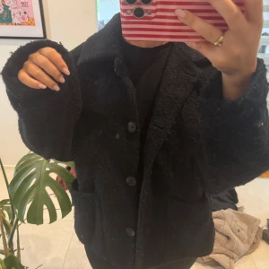 Svart teddyjacka med stora knappar - Säljer en svart teddyjacka med oversized passform och stora knappar framtill. Jackan har bred krage, två stora fickor och är långärmad. Perfekt för dig som gillar en chill och trendig look.