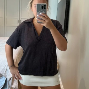 Mörkbrun tröja från H&M - Säljer en mörkbrun tröja från H&M i storlek L. Toppen har en djup v-ringning, krage och korta ärmar. Materialet är ribbad polyester som ger en chill och avslappnad vibe. Perfekt för dig som gillar enkel och stilren look.