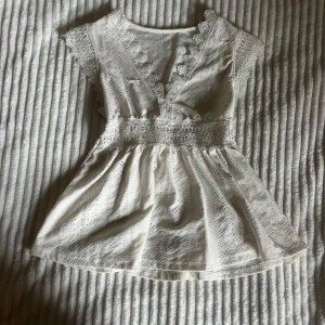 Vit spetsblus med volang - Superfin vit blus med v-ringning, dekorerad med spetsdetaljer och broderade mönster. Korta ärmar med spetskant och markerad midja som ger en söt och romantisk look. Perfekt för sommarens alla tillfällen!