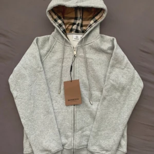 Grå Burberry hoodie med rutig huva - Snygg grå Burberry hoodie i storlek M. Klassisk dragkedja framtill och huva nyskcik