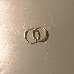 Guldiga hoops örhängen - Säljer ett par klassiska guldiga hoops örhängen i enkel och stilren design. Perfekta cirklar som ger en clean look och passar till allt. Lätta att bära och enkla att matcha med andra smycken.