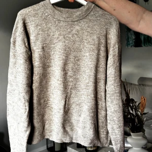 Beige stickad tröja med rund hals - Mysig beige stickad tröja med rund halsringning och ribbade muddar. Tröjan har en enkel och stilren design, perfekt för lager-på-lager och chill dagar. Långärmad och i mjukt material som känns skönt mot huden. ( Har ett hål i armhålan )