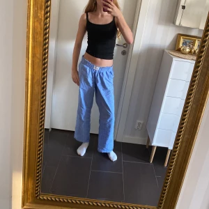 Blå randiga linnebyxor från Gina - Säljer ett par chill blå linnebyxor från Gina tricot med vita ränder. De har elastisk midja och raka ben, perfekta för en avslappnad stil. Lätta och luftiga, passar grymt bra till sommaren.