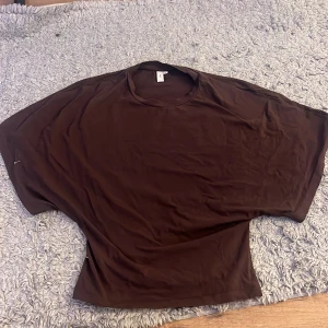 Brun loose topp från Nelly - Säljer en brun topp från Nelly i storlek S. Modellen är loose fit med breda, korta ärmar och rund halsringning. Materialet är mjukt och känns som bomull, perfekt för en chill och avslappnad stil. Enkel och stilren design utan mönster eller detaljer. Den är använd typ 3 gånger men i ett bra skick. Den ser mycket större ut än vad den är