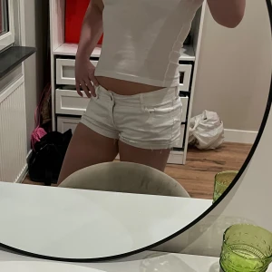 Vita lågmidjade jeansshorts från Hollister - Säljer ett par vita jeansshorts med låg midja och klassisk femficksdesign. Shortsen har råa kanter vid bensluten och stängs med dragkedja och knapp framtill. Perfekta för varma dagar och har en snygg, tight passform.