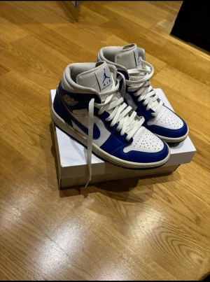 Nike Air Jordan 1 blå och vita sneakers - Nike Air Jordan 1 sneakers i blått och vitt med klassisk high-top siluett. Skorna har perforerad tå, snörning och ikoniska Jordan-loggor på sidan och plösen. Tillverkade i skinn med vit sula och blå detaljer, PRIS KAN DISKUTERAS TVEKA INTE!!