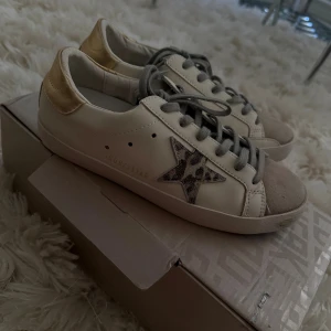 Golden Goose - Helt underbara gyllene gåsskor i storlek 39! Leopardmönstrad stjärna och guldfärgad metallic baksida, där texten har slitits bort naturligt. Skorna ser riktigt bra ut på utsidan och är annars i gott skick förutom det naturliga slitaget på sulorna! Ett typiskt problem med gyllene gåsskor är slitage på sulorna, vilket har hänt även med dessa, men det är mest märkbart på skospetsen. Spetssulorna har limmats fastare, men en skomakare skulle nog veta hur man åtgärdar problemet bättre. ❤️