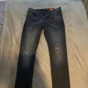 Svarta jeans från Cars Jeans med slitningar - Svarta jeans från Cars Jeans med coola slitningar och små vita detaljer på både fram- och baksida. Modellen är smal och har klassisk femficksdesign. Jeansen har knapp och dragkedja i midjan samt diskret logga på bakfickan.