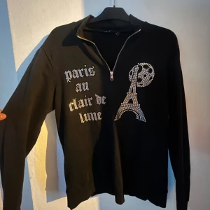 Blinglucid tröja half zip - Svart långärmad tröja med half zip och strassdetaljer som bildar texten 'paris au clair de lune säljer tröjan då den inte används längre 