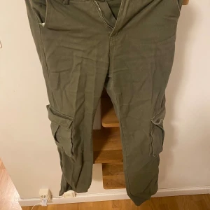 Olivgröna cargopants från Shein XS - Snygga olivgröna cargopants från Shein i storlek XS. Byxorna har flera praktiska fickor på benen och bak, klassisk cargostil och är tillverkade i mjuk bomull. Perfekt för dig som gillar streetwear och utility-vibe.
