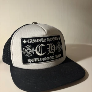 Chrome Hearts keps - Snygg truckerkeps från Chrome Hearts i svart och vitt med broderad patch framtill och metallknapp på toppen. Kepsen har mesh på sidorna och bak, samt böjd skärm. Broderad text och detaljer i vitt på svart bakgrund.