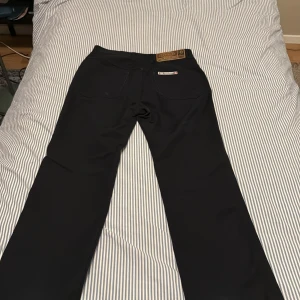 Bootcut jeans från Psycho International - Svarta byxor från Psycho International med klassisk bootcut-passform. Snyggt raka ben och diskret design med knappstängning och fickor både fram och bak. Materialet känns slätt och har en stilren look som funkar till många olika outfits. För övriga frågor skriv privat😀