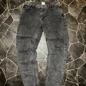 Gråa Grunt Jeans - Snygga svarta jeans från Grunt Organic med klassisk femficksdesign och knappstängning. Jeansen har en rak passform och är tillverkade i ekologisk bomull. Perfekt för dig som gillar en enkel och stilren look med lite tvättad finish.