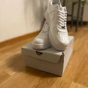 Nike Air Force 1 '07 helvita sneakers - Nike Air Force 1 '07 i helvitt skinn, klassisk low-top modell med perforerad tå, rund tå och snörning. Snygg och clean siluett som passar till allt. Ikonisk Swoosh-logga på sidorna och platt sula för skön komfort.