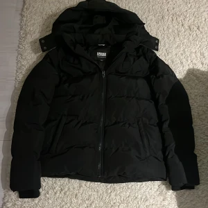 Svart pufferjacka Urban Classics - Svart pufferjacka från Urban Classics med huva och dragkedja framtill. Jackan har en clean look perfekt nu inför vintern❄️jackan kostar runt 1200kr ny pris✅skicket är 10/10 inget fel på den och inga defekter. Passar dig som är mellan 165-175.🤩går även att sänka priset vid snabb affär💰bara höra av sig vid funderingar.😊