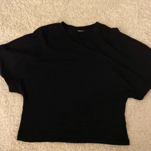 Svart croppad topp med kort ärm - Svart croppad topp från Gina tricot  med rund hals och korta ärmar. Enkel och stilren design i mjukt bomullsmaterial, perfekt att matcha med jeans eller kjol. Snygg passform som sitter normalt och ger en clean look.