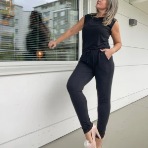 Svart jumpsuit med snörning - Mårk grå,nästan svart jumpsuit med smal passform och snörning i midjan. Mjukt material, viskos och har fickor på sidorna. Ärmlös överdel och långa ben som sitter tight. Perfekt för en chill och stilren look.