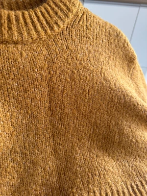 Croppad senapsgul stickad tröja H&M - Croppad stickad tröja från H&M i en snygg senapsgul färg. Tröjan har grov ribbad kant vid hals, ärmslut och nederkant, samt långa ärmar och relaxed passform. Materialet är en mix av polyester, ull, alpacka och elastan för en mjuk och skön känsla. Senapsgul stickad långärmad kortare / semi croppad tröja. Storlek XS-S. Gul / orange / brun. 