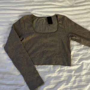 Ribbad croppad topp från H&M - Säljer en ribbad croppad topp från H&M i beige färg. Toppen har lång ärm, fyrkantig ringning och är tillverkad i en stretchig blandning av polyester, polyamid och elastan. Perfekt för dig som gillar en enkel men trendig look.