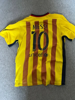 Barcelona Messi 10 gul matchtröja - Gul FC Barcelona fotbollströja från Nike med Messi 10-tryck på ryggen. Framsidan har Qatar Airways-logga och klubbmärke, baksidan har röda vertikala ränder och UNICEF-tryck. Kortärmad, tillverkad i lätt Dri-Fit material som andas. Perfekt för dig som älskar Barca och Messi.