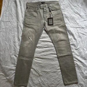 Slim grå jeans från Tom Ford, stl 34 - Slim fit jeans från Tom Ford i en snygg ljusgrå nyans. Klassisk femficksmodell med knappgylf och diskreta silverfärgade knappar. Tillverkade i mjukt bomullsmaterial för en bekväm känsla. Endast använda en gång. Ny pris 8499kr köpta på NK