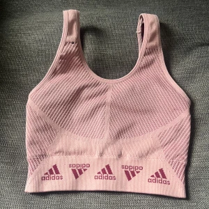 Adidas rosa träningstopp - Säljer en aldrig använd Adidas Aeroknit träningstopp i färgen Wonder Mauve med vinröda loggor längs nederkanten. Toppen är ribbad och sömlös med breda axelband och sportig look. Perfekt för gymmet eller löpning, superstretchig och bekväm.