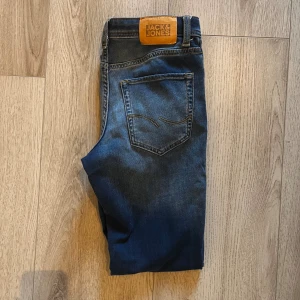 Jack & Jones Slim Glenn Jeans - Snygga blå jeans från Jack & Jones med klassisk femficksdesign och brunt läderpatch bak i midjan. Jeansen har en slim passform och är tillverkade i mjukt denimtyg med lätt tvättad look. Perfekta för dig som gillar stilrena och tidlösa jeans.