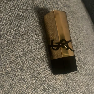 YSL rosa läppstift P22 - Säljer ett lyxigt läppstift från Yves Saint Laurent i färgen P22. Hylsan är guldig med svart YSL-logga och själva läppstiftet är en snygg, matt bubbelgumsrosa nyans. Klassisk fyrkantig form och exklusiv känsla, perfekt för dig som vill sticka ut.