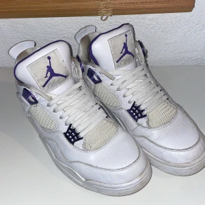 Nike Air Jordan 4 Retro vit/lila - Säljer ett par Nike Air Jordan  i vitt skinn med lila detaljer och klassisk Jumpman-logga på plös och häl. Skorna har meshpaneler, snörning och en chunky sula. Insidan är fodrad i lila tyg för extra kontrast. Perfekta för dig som gillar streetwear och sneakers med attityd.