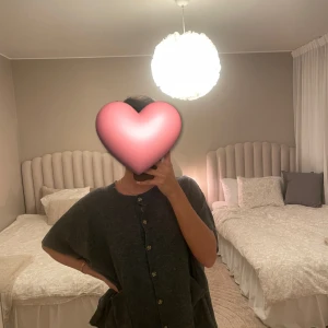 Grå stickad t-shirt från Masai - Mysig grå stickad T-shirt från Masai med korta ärmar, knappar framtill och två stora fickor. Avslappnad passform och rund halsringning. Perfekt för dig som gillar en chill och enkel stil.