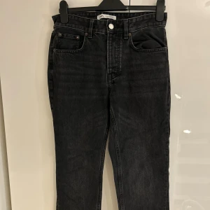 Svarta raka jeans från Zara - Snygga svarta jeans från Zara i klassisk femficksmodell med raka ben och normal passform. Jeansen har hög midja, silverfärgad knapp och detaljerade sömmar. Perfekt för dig som gillar en enkel och stilren look.