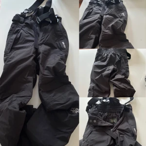 Svarta skidbyxor Peak Performance XS - Svarta vintage skidbyxor från Peak Performance med GORE-TEX-material och justerbara hängslen. Byxorna har elastisk midja, dragkedjor vid fickorna och logga på benet. Perfekta för vintern och outdoor-aktiviteter. Snygg och funktionell design. Inköpta i Trysil