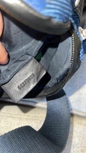 Hugo Boss - Snygg mörkblå axelväska från Hugo Boss sällsynt modell, med justerbar rem och tydlig logga på framsidan. Väskan har dragkedja upptill och detaljer i svart, samt en grön etikett på insidan. Materialet är slitstark polyester med inslag av skinn vid kanterna.