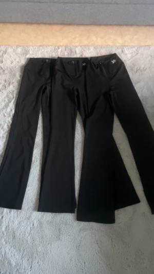 Svarta bootcut träningsbyxor från Lager 156 - Säljer tre par svarta bootcut träningsbyxor från Laget 156. Byxorna har hög midja, dragkedjor framtill och är gjorda i ett stretchigt syntetmaterial som passar perfekt för sportiga aktiviteter. Snyggt logotryck på höften och stilren design.