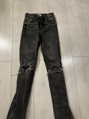 Svarta ripped jeans från Zara - Jag säljer nu mina jeans från Zara. Hål på knäna, tajt passform med slit längst ner. Bra skick och inte mycket använda. Storlek 34. 