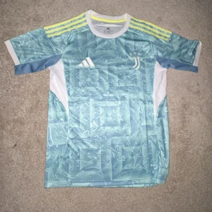 Juventus blå kortärmad fotbollströja - Juventus fotbollströja från Adidas i slim fit, med ljusblå och vita vattenmönster, gula ränder på axlarna. (Ny med prislapp)