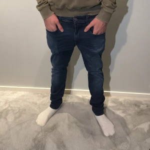 Replay Anbass jeans mörkblå tapered - Snygga mörkblå Replay Anbass jeans med tapered passform och klassisk femficksdesign. Jeansen har en cool tvätt, tydliga sömmar och Replay-logga på fickan. Materialet är stretchigt jeans och midjan är normal. Perfekt för dig som gillar streetstyle. Modellen är 190cm lång och väger 75kg 