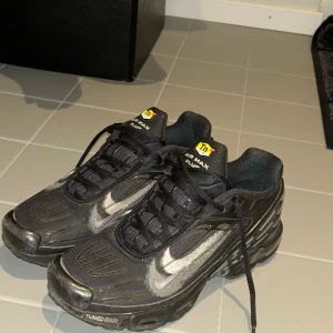 Nike Air Max Plus Tn Svarta Sneakers - Nike Air Max Plus Tn sneakers i svart med silvriga detaljer och klassisk Tn-logga på plösen. Skorna har snörning, platt sula och Tuned Air-dämpning för extra komfort. Materialet är syntet med mesh-paneler och gummisula. Snyggt futuristiskt mönster längs sidorna och bak. Är i bra skick.