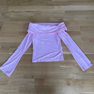 Rosa offshoulder topp från ASOS - Säljer en ljusrosa offshoulder topp från ASOS DESIGN. Toppen har långa ärmar och en bred, nedvikt krage som ger en snygg och trendig look. Materialet är mjukt och stretchigt, troligen bomull eller polyester. Perfekt för dig som gillar pastellfärger och vill sticka ut.