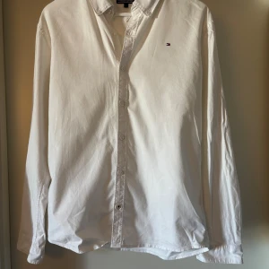 Vit skjorta från Tommy Hilfiger - Vit skjorta från Tommy Hilfiger med klassisk krage och diskret logobrodyr på bröstet. Skjortan har lång ärm, knappar framtill och är gjord i mjuk bomull. Perfekt för en clean look.