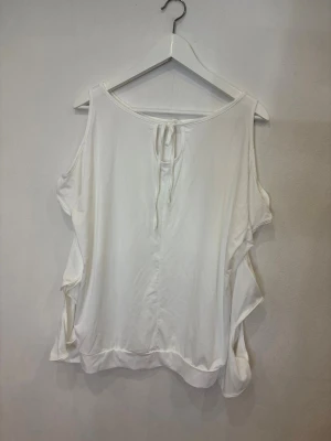 Vit ärmlös linnetopp med knyt - Säljer en vit ärmlös linnetopp med snygga volangdetaljer längs sidorna och knytning i nacken. Toppen har en lös passform och är tillverkad i ett mjukt, lätt material som känns skönt mot huden. Perfekt för varma dagar när du vill ha en chill och stilren look.